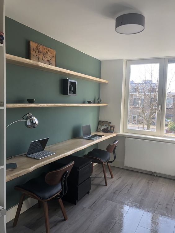 an office with two desks and shelves on the wall, in front of a large window