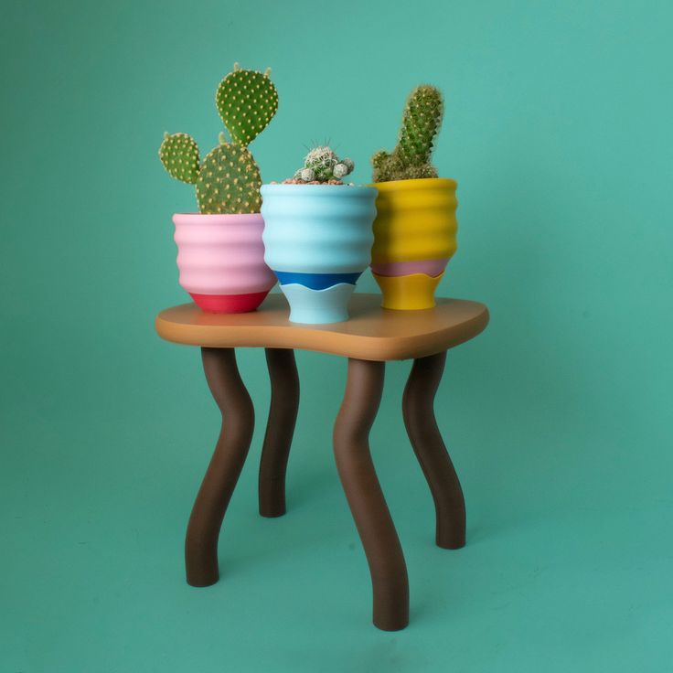 three different colored pots with cactus plants in them on a small table against a green background