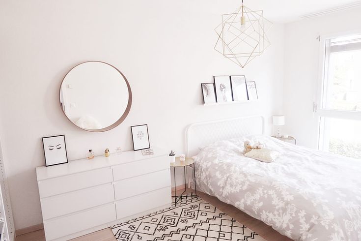 a bedroom with a bed, dresser and large round mirror on the wall above it