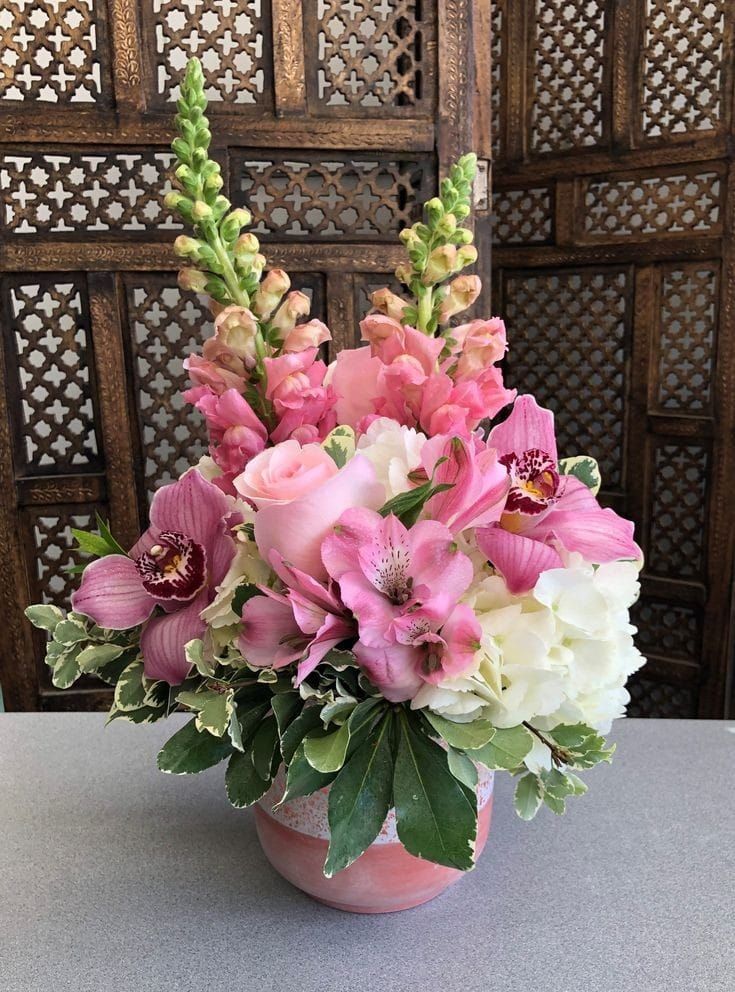 a pink vase filled with lots of flowers on top of a table