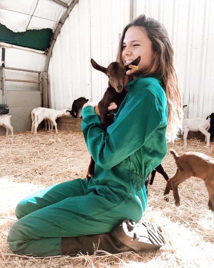 a woman in green jumpsuit holding two baby goats