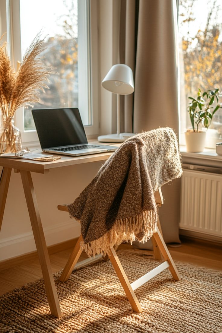 a laptop computer sitting on top of a wooden desk next to a window covered in a blanket