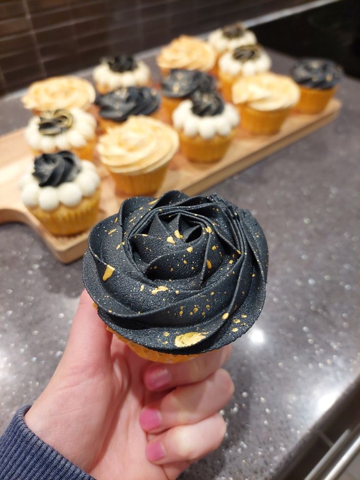 a hand holding a cupcake with black and white frosting in front of other cupcakes