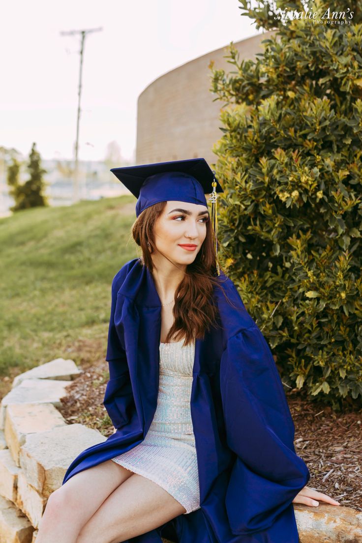 a woman sitting on top of a stone wall wearing a graduation cap and gown with her legs crossed