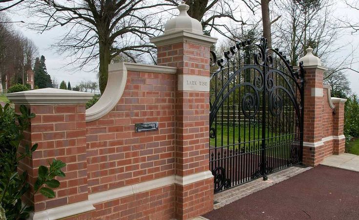 a brick fence with an iron gate in front of it and trees on the other side