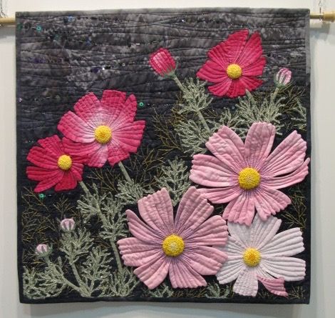 pink and white flowers are displayed on a black quilted wall hanging from a rope