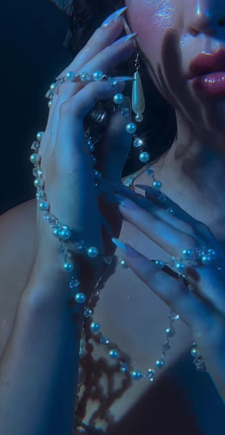 a woman with blue makeup holding a cell phone to her ear and wearing pearls around her neck