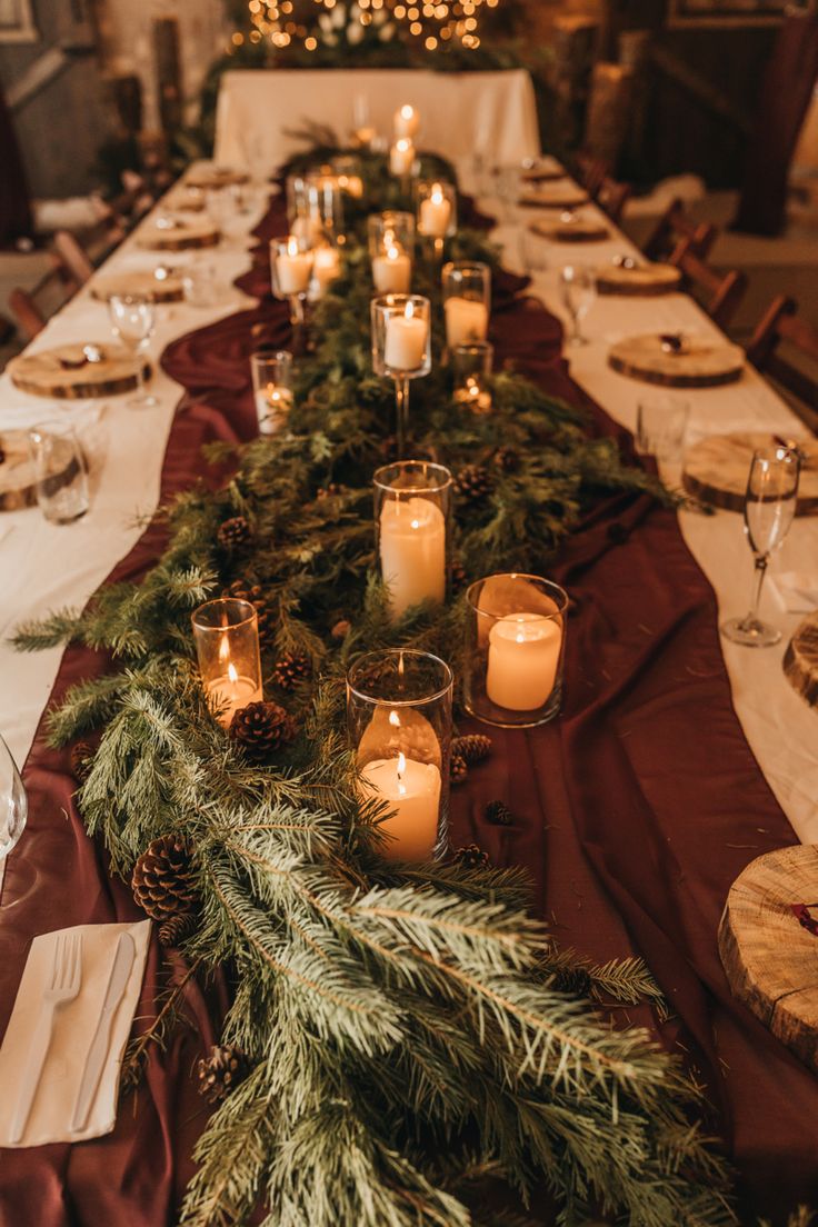 a long table is set with candles and evergreen garland for a festive dinner party