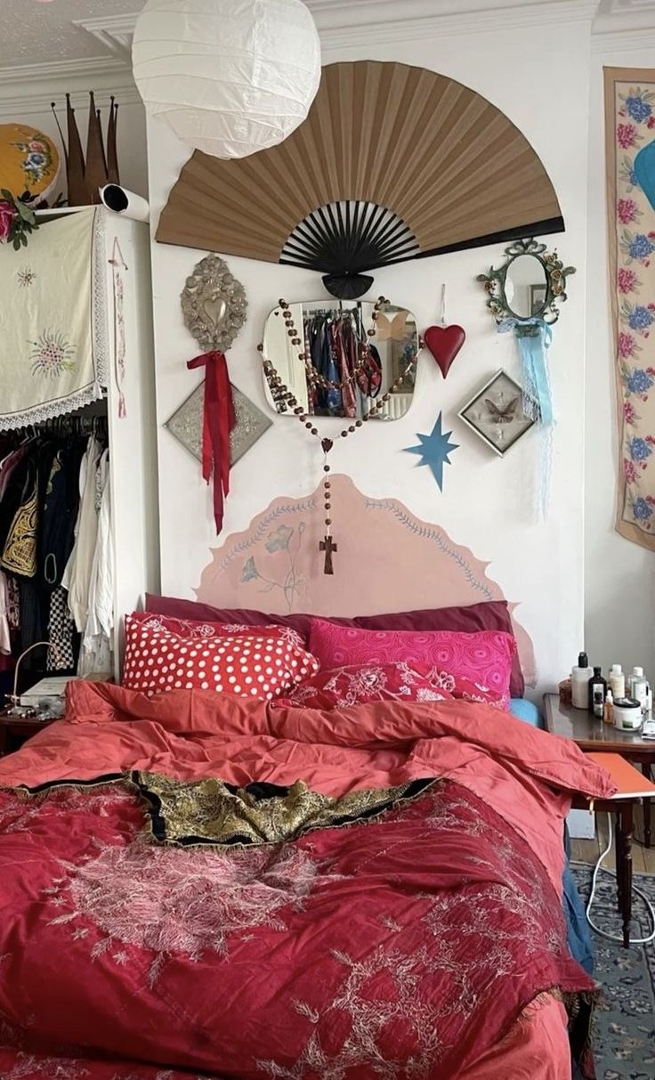 a bed with red comforter and pillows in a room filled with pictures on the wall