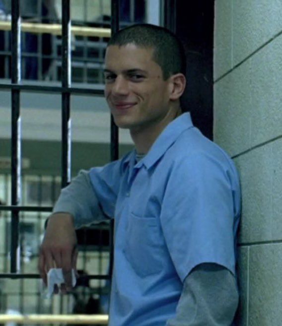 a man leaning against a wall with his hand on the door handle and smiling at the camera