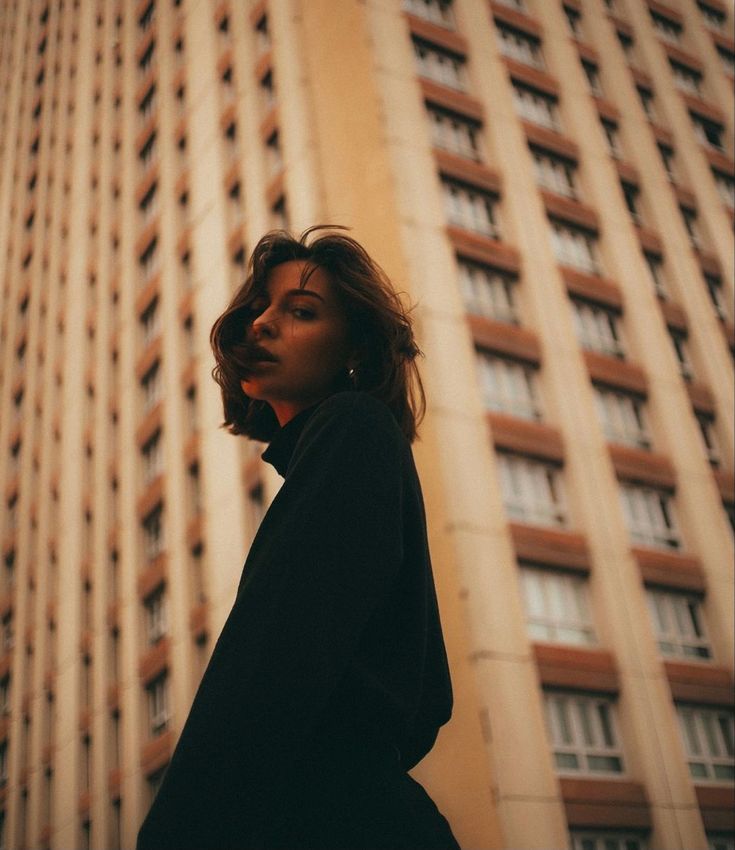 a woman standing in front of a tall building with her head turned to the side