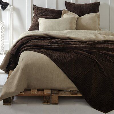 the bed is made up with brown linens and pillows on wooden pallets in front of a white wall