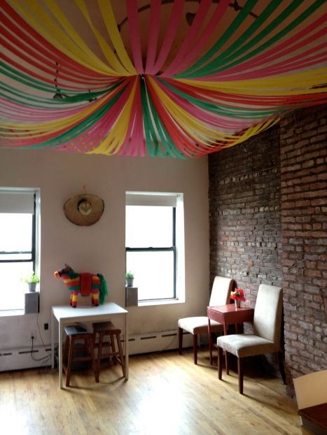 a room with some chairs and tables under a colorful drape on the ceiling in front of two windows