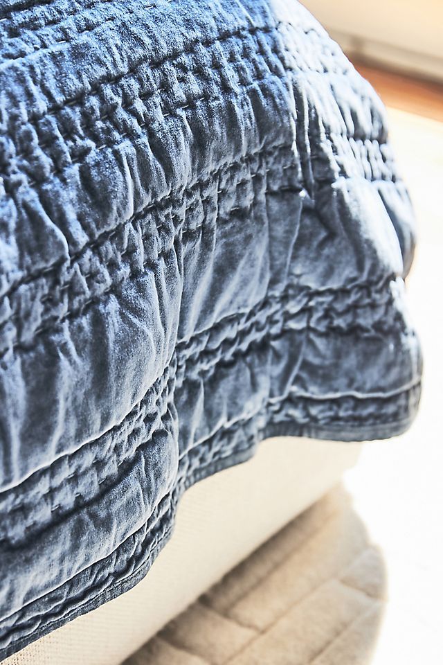 a close up view of a blue quilted pillow on top of a white bed