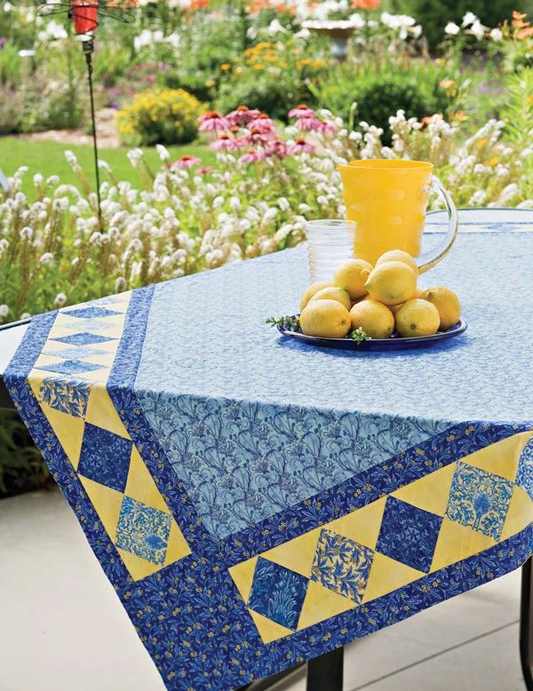 a blue and yellow table cloth with lemons on it in the middle of a garden