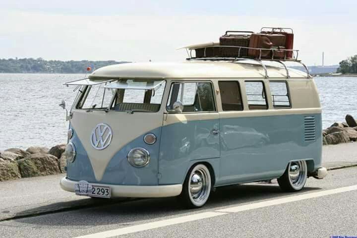 an old vw bus with luggage on top is parked by the water in front of some rocks