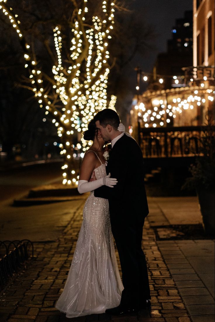 a bride and groom standing in front of a tree with lights on it at night