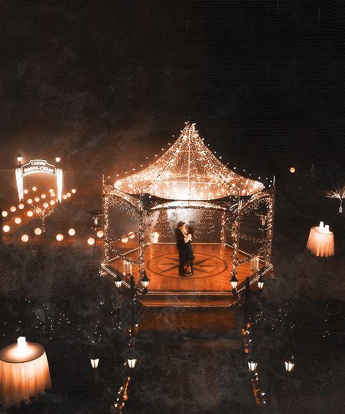 a man and woman standing in front of a lit up gazebo with lights on it