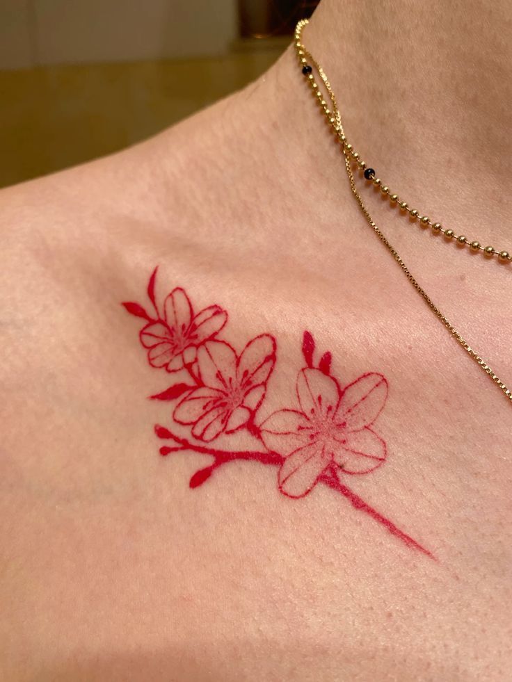 a woman's chest with a red flower tattoo on her left shoulder and gold chain