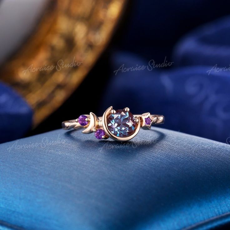 a ring with three stones on it sitting on top of a blue cushion