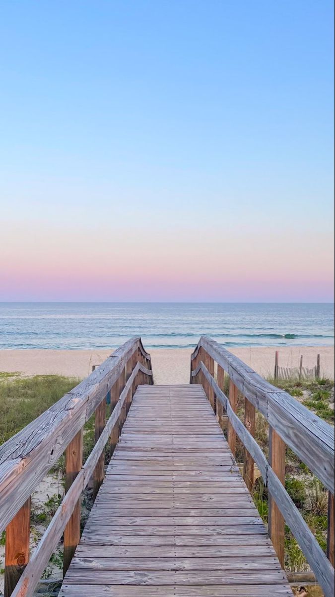 a wooden walkway leading to the beach at sunset