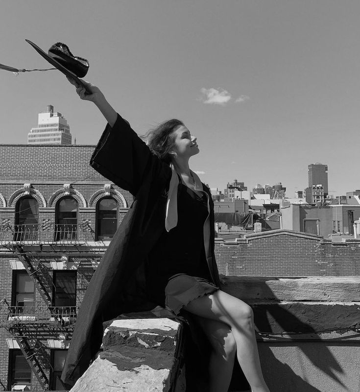 a woman sitting on top of a building holding a hat