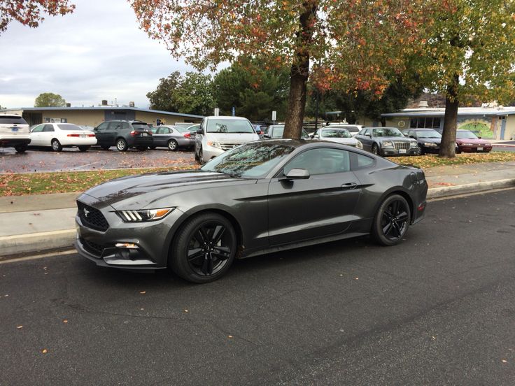 a gray mustang parked on the side of the road in front of a parking lot