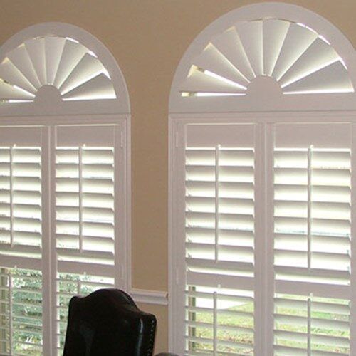 three arched windows with white shutters in an empty living room, along with a black leather chair