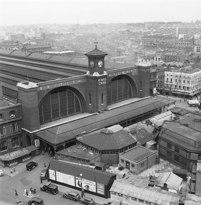 black and white photograph of an old train station with cars parked in the parking lot