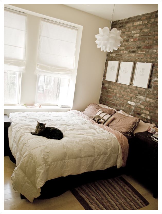 a cat laying on top of a white bed in a bedroom next to a brick wall