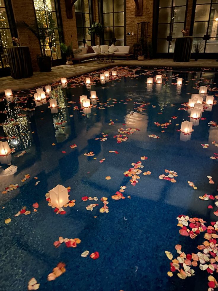 many lit candles are floating on the water in this pool filled with flowers and petals