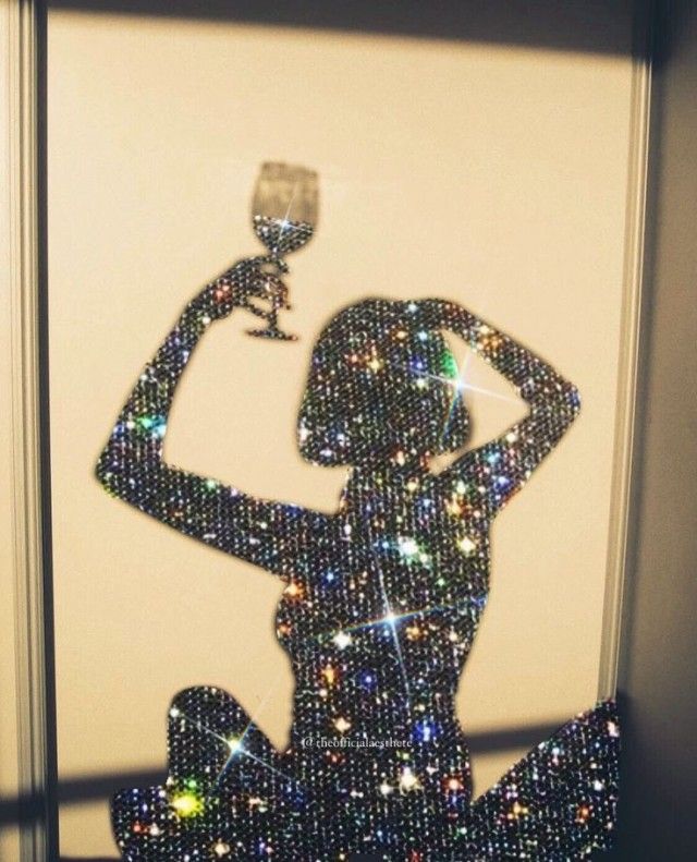 a woman sitting on the floor holding a wine glass in front of her face with glitters all over it