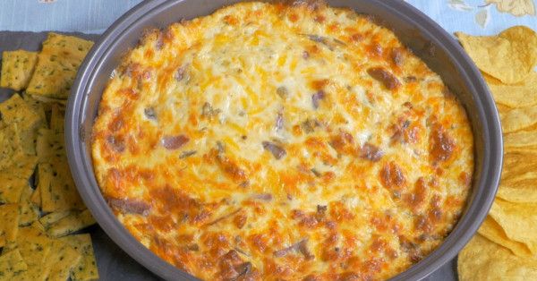 a cheese dip with tortilla chips on a slate platter next to it