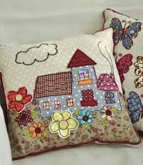 two decorative pillows on a bed with white linens and colorful embroidered houses in the background