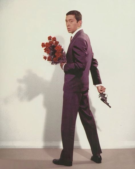 a man in a suit and tie holding a bouquet of flowers while standing against a wall