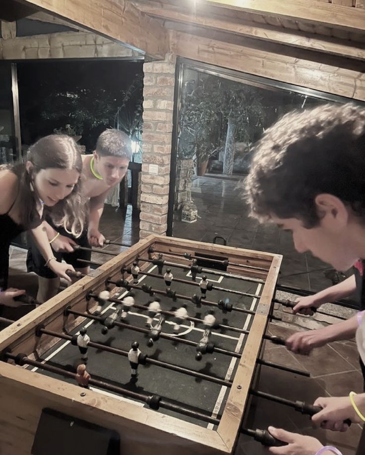 three people are playing with an old foo - ball table