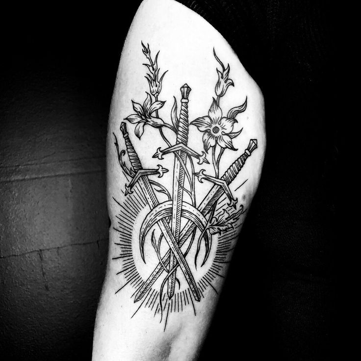 a black and white photo of a tattoo on the arm with swords, flowers and stars