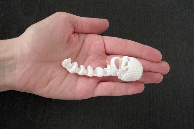 a hand holding a small white crocheted object