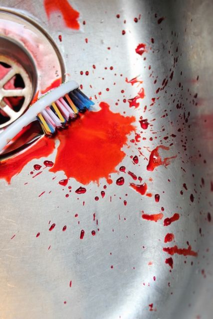 a toothbrush with red paint on it sitting in a sink