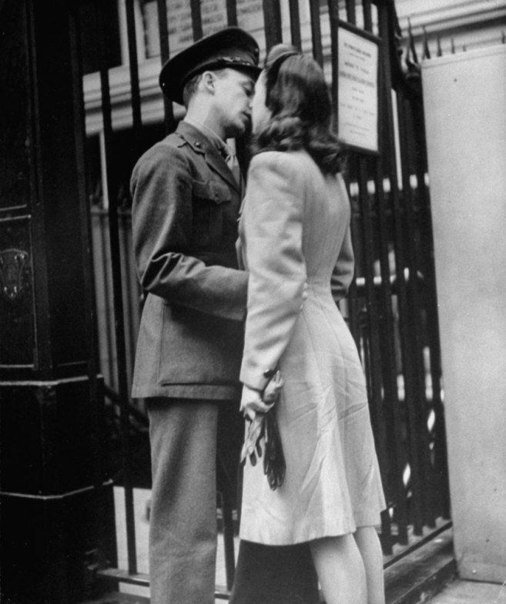 a man and woman are kissing in front of a train station sign while standing next to each other