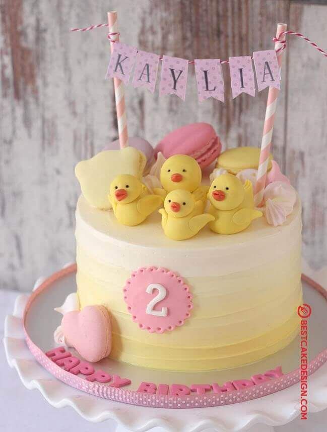 a birthday cake decorated with yellow rubber ducks and pink icing, on a white plate