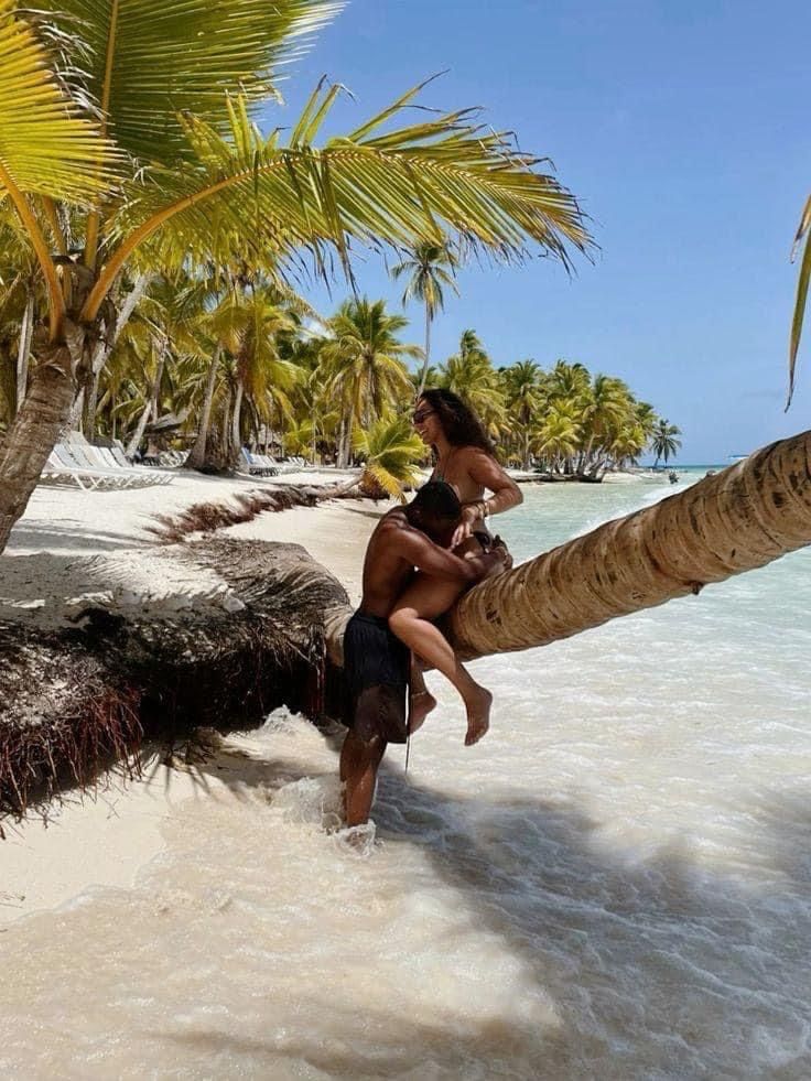 a woman is sitting on a palm tree at the beach and she is holding her baby