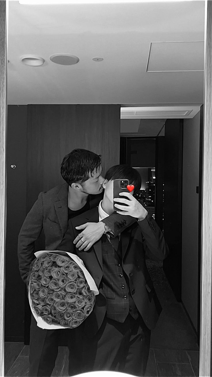 a man and woman kissing while taking a selfie in front of a mirror with roses on it