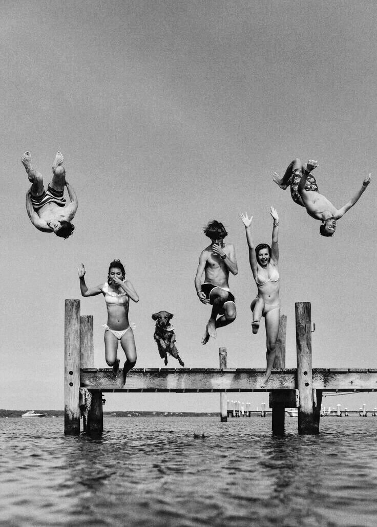 four people jumping off a pier into the water