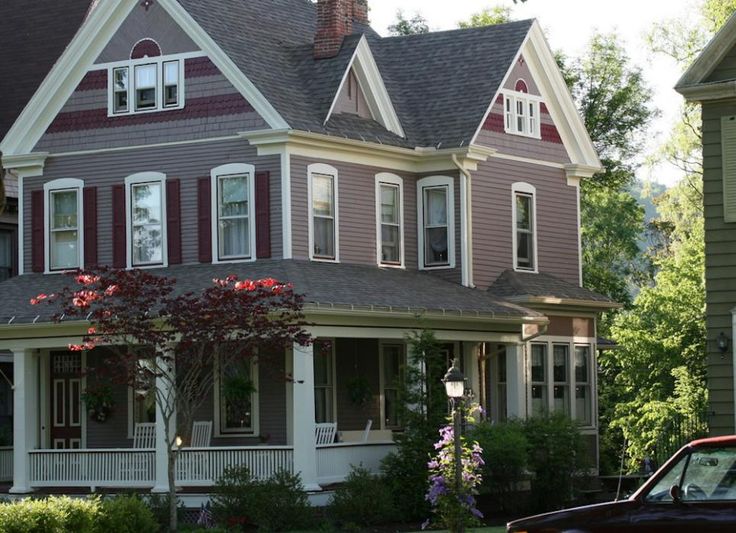 a car is parked in front of a house with red shutters and white trim