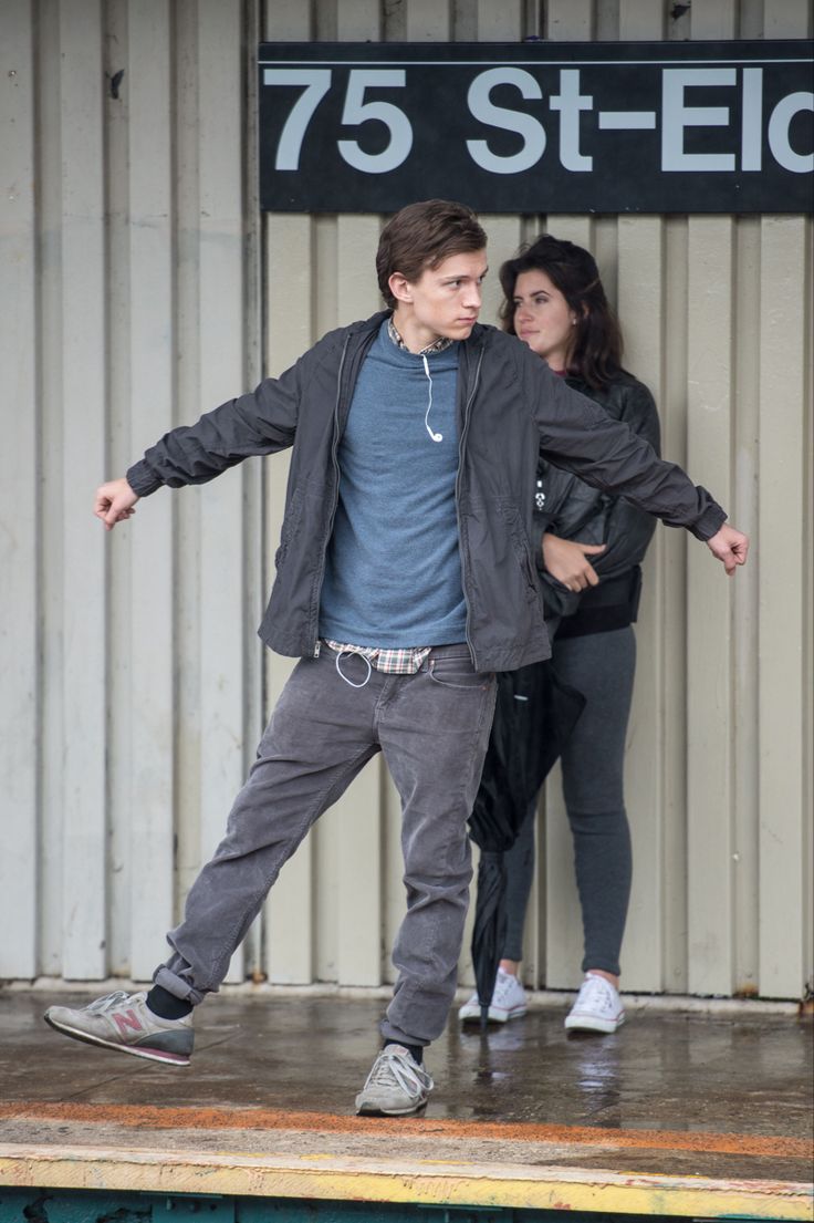 a young man and woman are standing on the side of a train platform with their arms outstretched