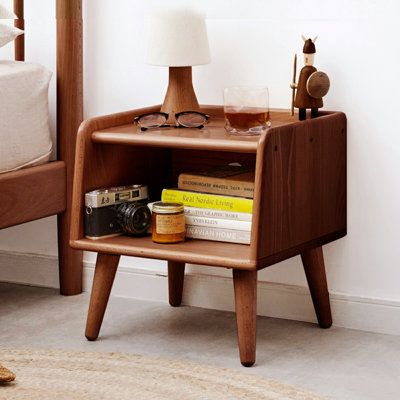 a small wooden shelf with books and glasses on it next to a bed in a bedroom