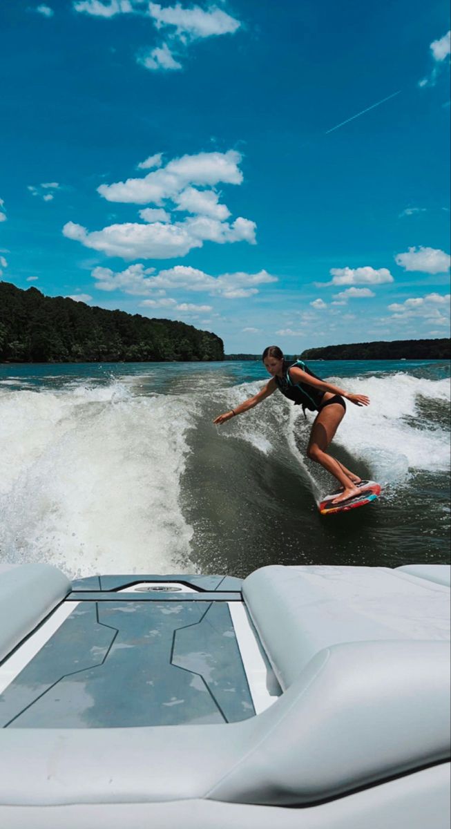 a person on a surfboard in the water near a boat and some hills with trees