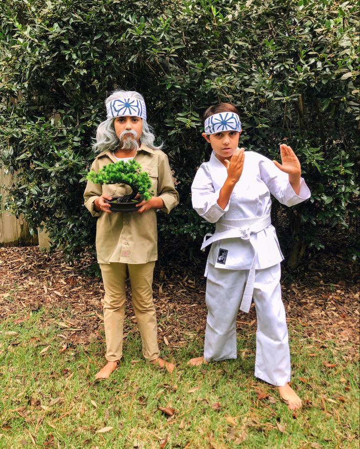 two people dressed in costumes standing next to each other on the grass with plants and trees behind them