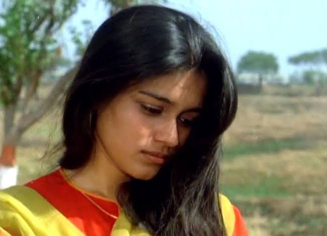 a young woman in a yellow and red shirt looking at her cell phone while standing next to a tree